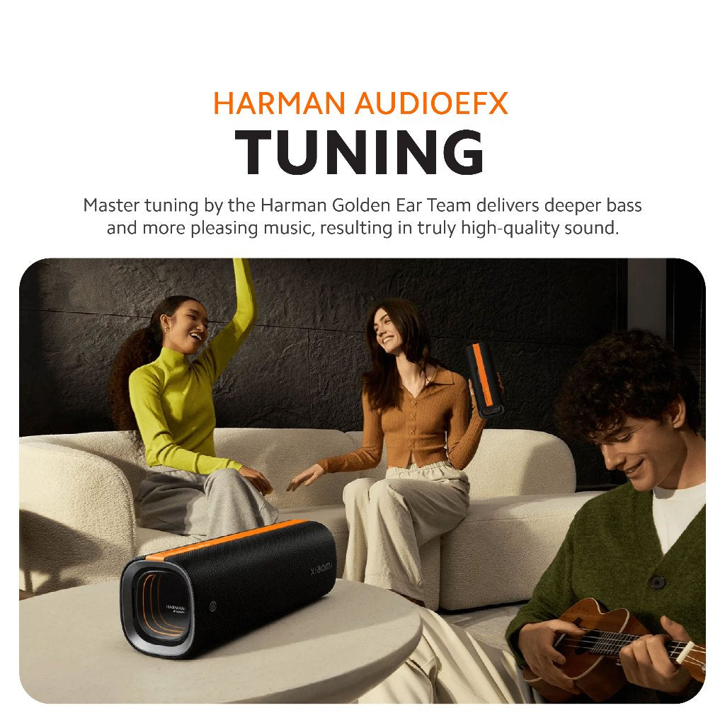 Black portable Bluetooth speaker with orange trim on a couch near people