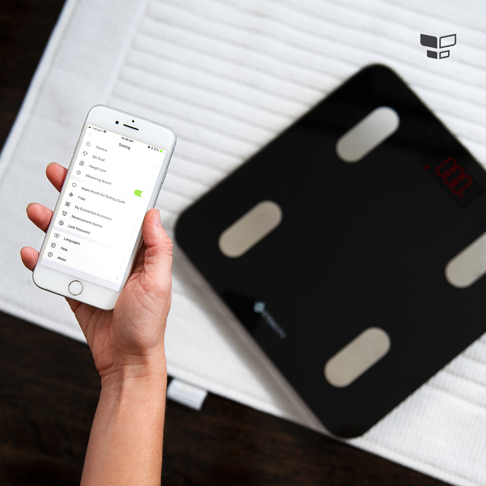 Body fat scale with red LCD and a hand holding a phone app
