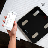 Body fat scale with red LCD and a hand holding a phone app